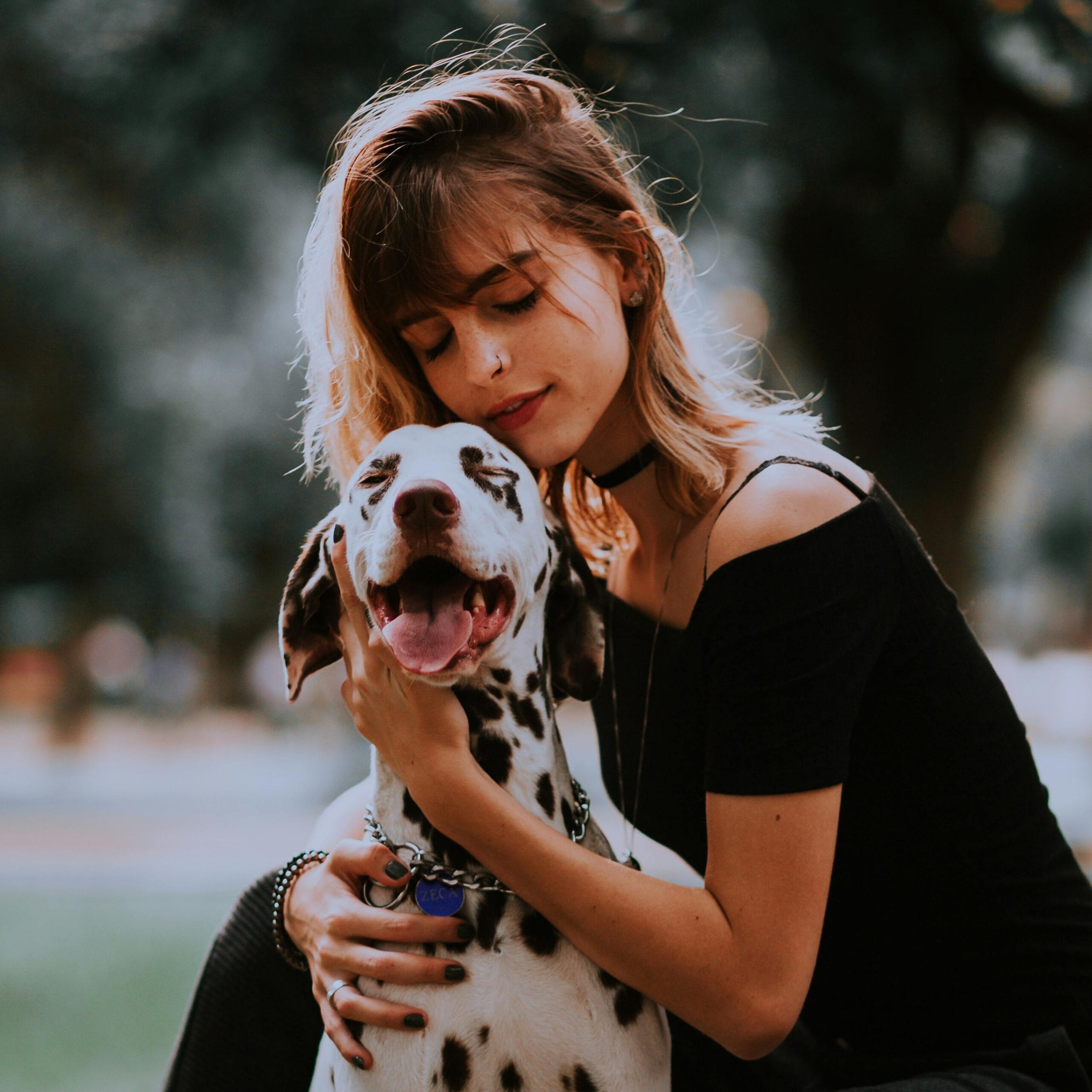 A young woman hugging her Dalmatian dog in a park, showcasing friendship and joy.